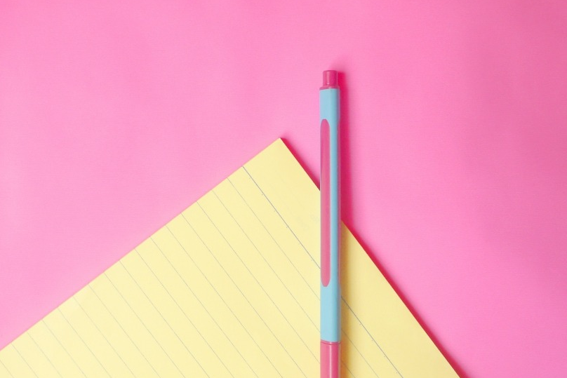 A notebook and pen on a pink and sky blue color pen on pink background